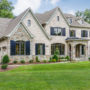 a traditional tan brick house with navy blue shutters