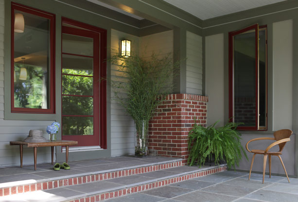 a traditional entry with sage green siding and red brick detailing