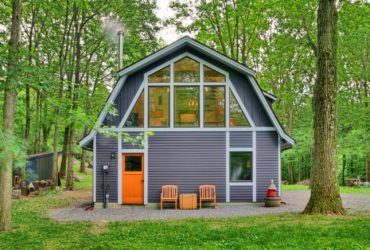 a barn-style house with grey siding, white trim, and orange front door