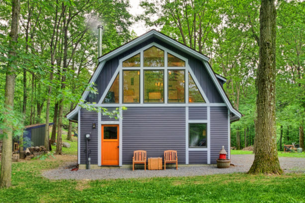 a barn-style house with grey siding, white trim, and orange front door